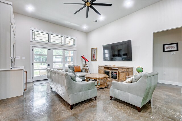 living room with ceiling fan, concrete flooring, french doors, and a towering ceiling