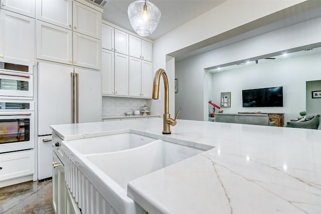 kitchen featuring decorative light fixtures, double oven, light stone counters, white cabinetry, and sink