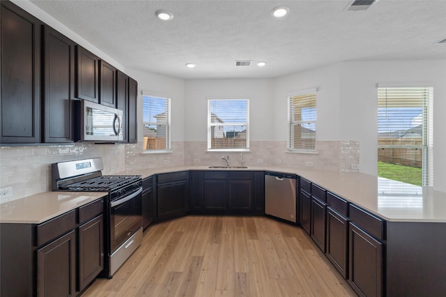 kitchen featuring backsplash, sink, light hardwood / wood-style floors, kitchen peninsula, and stainless steel appliances