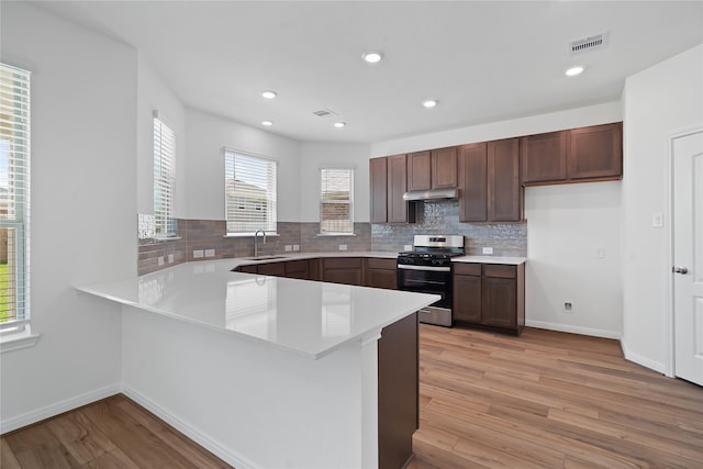 kitchen with stainless steel range, light hardwood / wood-style flooring, kitchen peninsula, and sink