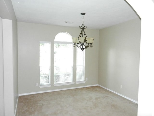 carpeted empty room featuring a chandelier