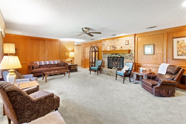 carpeted living room with wood walls, ceiling fan, a textured ceiling, and a fireplace