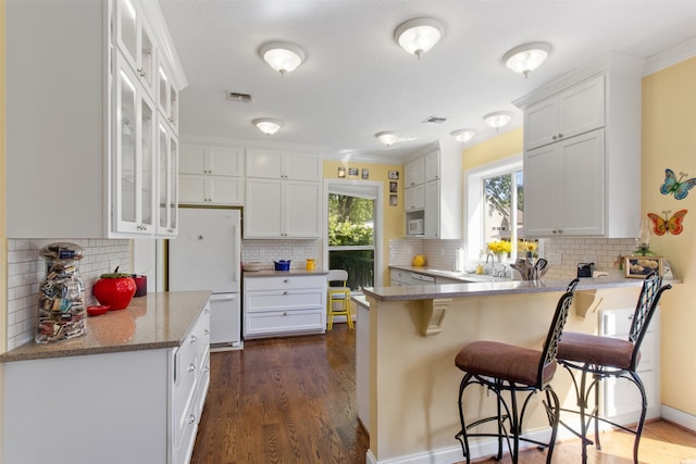 kitchen with white fridge, backsplash, white cabinetry, dark hardwood / wood-style floors, and kitchen peninsula