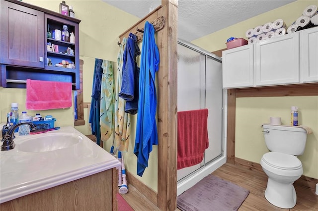 bathroom featuring wood-type flooring, toilet, a shower with door, and a textured ceiling