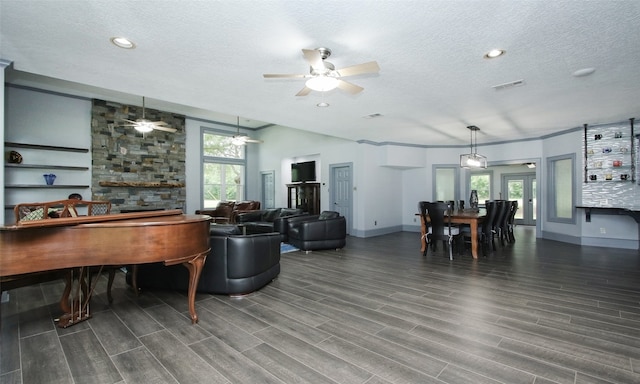 living room with dark hardwood / wood-style floors, ceiling fan, built in shelves, and a textured ceiling