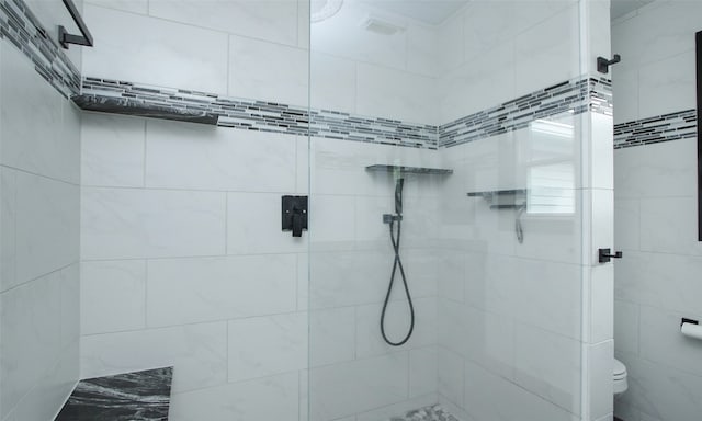 bathroom with a tile shower and toilet