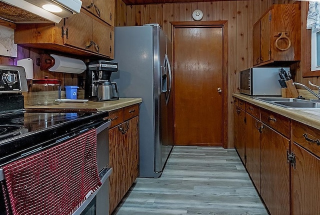 kitchen featuring appliances with stainless steel finishes, wood walls, sink, exhaust hood, and light wood-type flooring