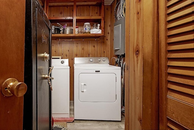 laundry area featuring washing machine and clothes dryer, electric panel, light wood-type flooring, and wood walls