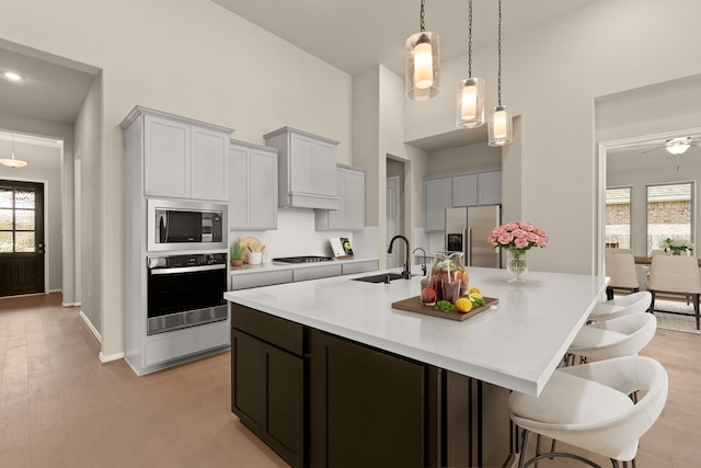 kitchen with stainless steel appliances, sink, light wood-type flooring, and an island with sink