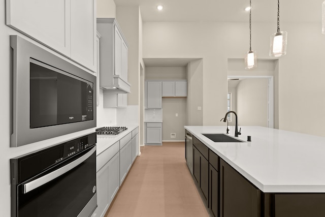 kitchen with sink, white cabinetry, stainless steel appliances, pendant lighting, and a center island with sink