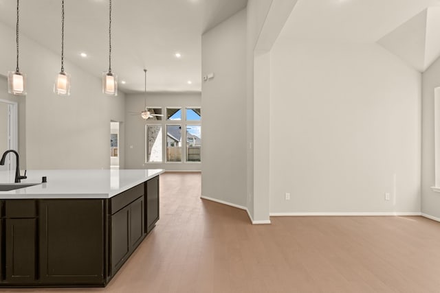 kitchen with a center island with sink, hanging light fixtures, ceiling fan, high vaulted ceiling, and light wood-type flooring