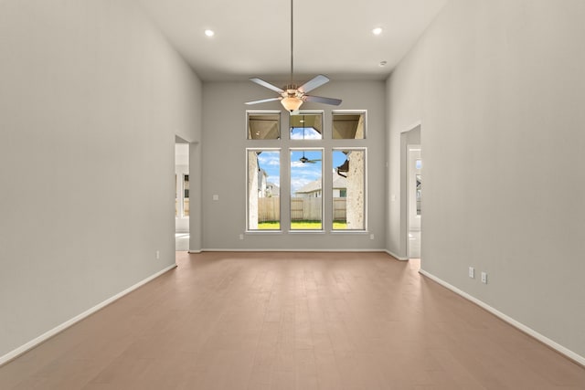 unfurnished living room with ceiling fan, a towering ceiling, and light wood-type flooring