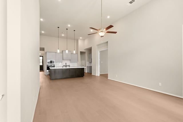 kitchen featuring a kitchen island with sink, hardwood / wood-style floors, built in microwave, sink, and pendant lighting