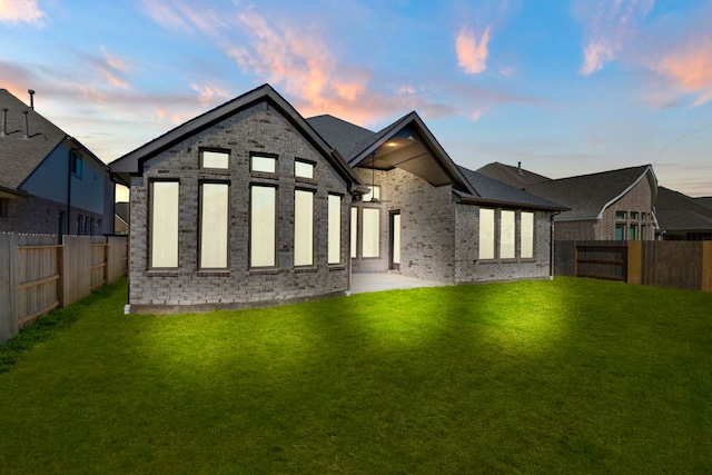 back house at dusk featuring a patio area and a yard