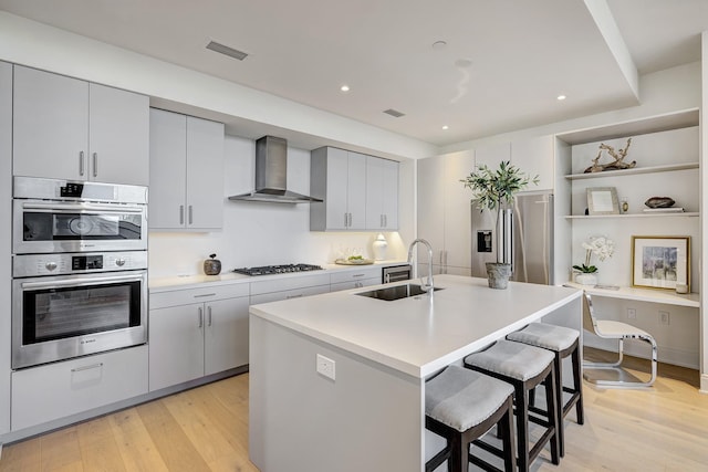 kitchen featuring a breakfast bar area, open shelves, a sink, appliances with stainless steel finishes, and wall chimney range hood