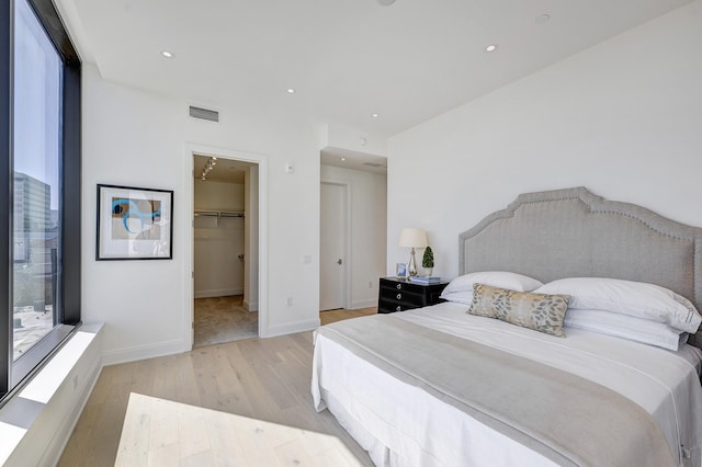 bedroom with baseboards, visible vents, light wood-style flooring, recessed lighting, and a walk in closet