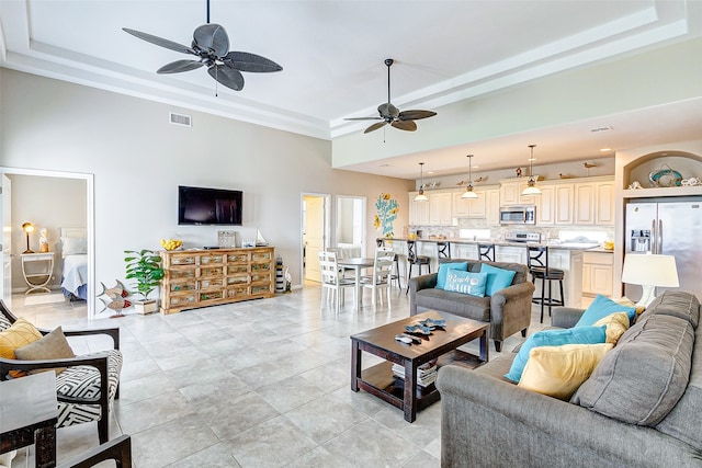 tiled living room with ceiling fan and a raised ceiling