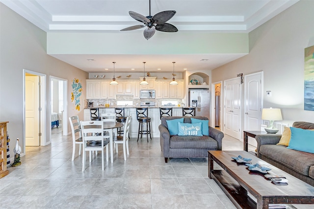 living room featuring a raised ceiling, ceiling fan, and light tile flooring