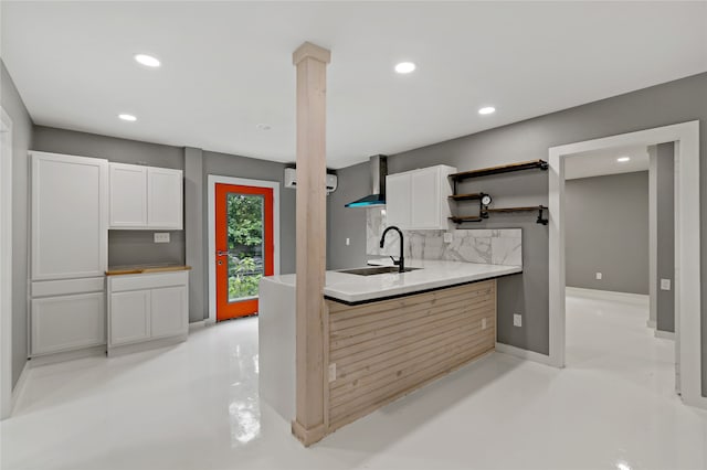 kitchen with wall chimney exhaust hood, sink, white cabinetry, and backsplash