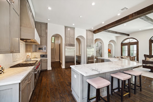 kitchen with built in appliances, premium range hood, a spacious island, dark wood-type flooring, and beam ceiling