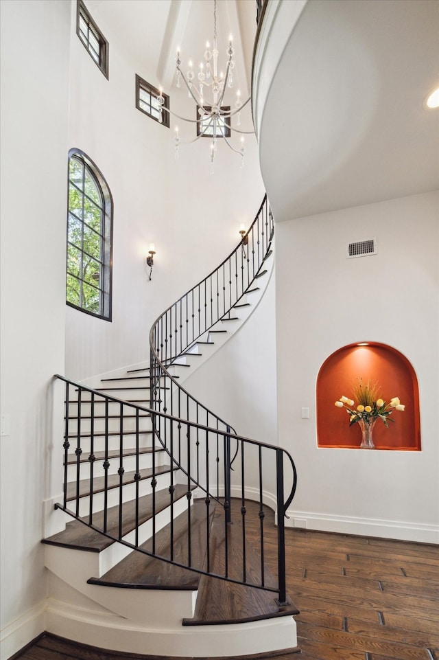 stairway featuring dark wood-type flooring, beam ceiling, a towering ceiling, and a notable chandelier