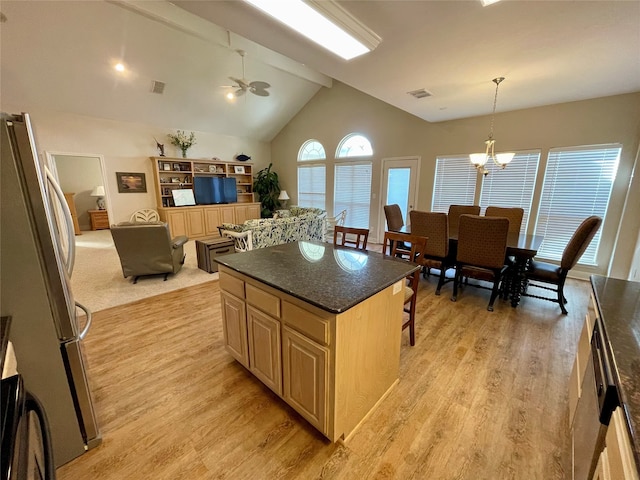 kitchen featuring ceiling fan with notable chandelier, a kitchen island, light colored carpet, stainless steel fridge, and lofted ceiling