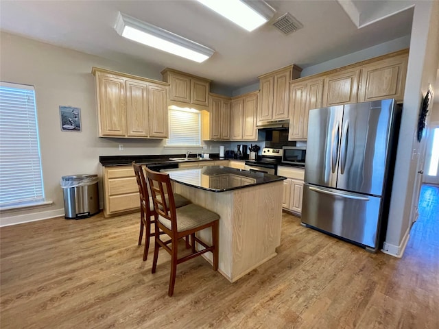 kitchen featuring light brown cabinets, light hardwood / wood-style flooring, stainless steel appliances, a kitchen breakfast bar, and a center island