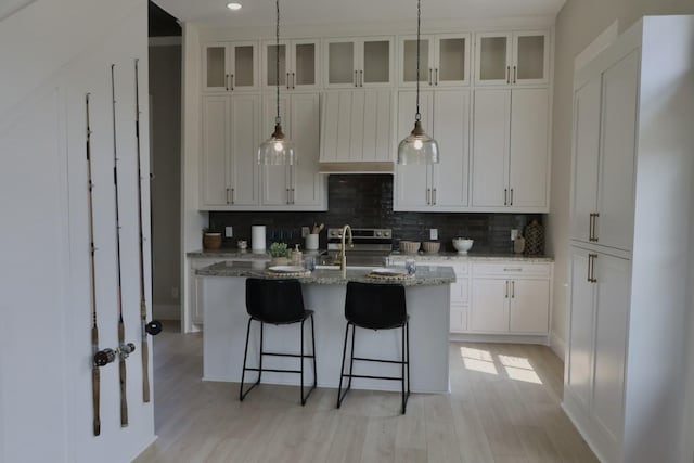 kitchen with light stone countertops, a breakfast bar, a kitchen island with sink, sink, and white cabinets