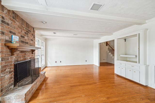 unfurnished living room featuring a fireplace, beamed ceiling, a textured ceiling, and light hardwood / wood-style flooring