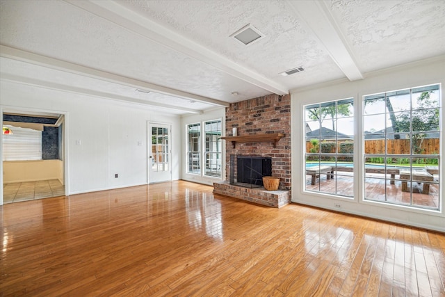 unfurnished living room with a fireplace, beamed ceiling, a textured ceiling, and light hardwood / wood-style flooring