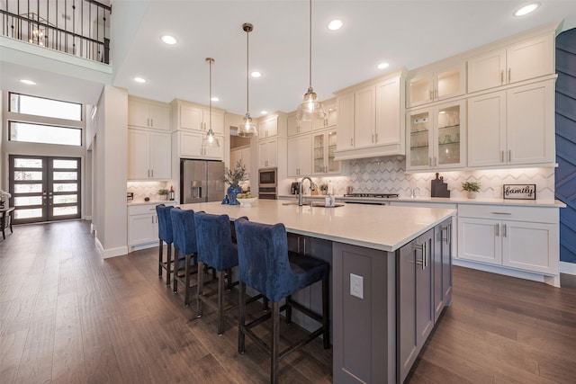 kitchen with appliances with stainless steel finishes, decorative light fixtures, sink, dark wood-type flooring, and a center island with sink