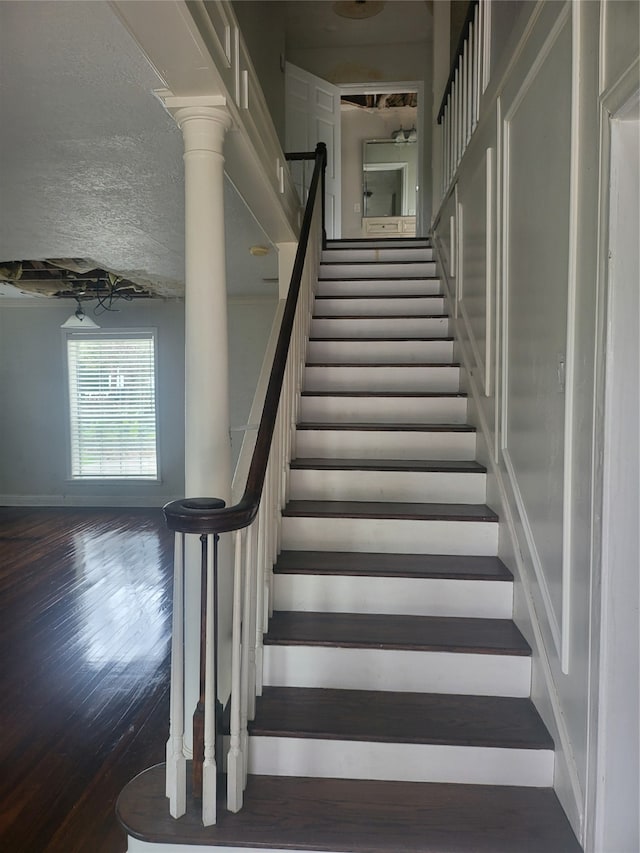 staircase featuring dark wood-type flooring and decorative columns