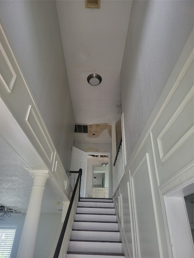 staircase featuring a textured ceiling and ornate columns