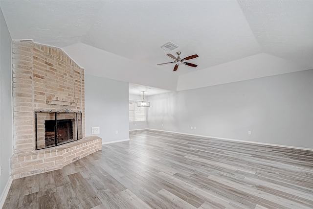 unfurnished living room with ceiling fan, light hardwood / wood-style floors, a raised ceiling, and a brick fireplace