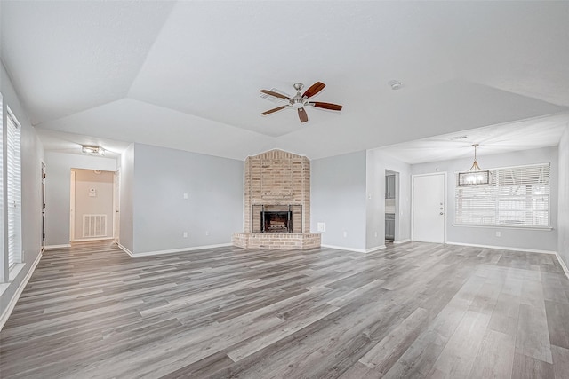 unfurnished living room featuring a fireplace, light wood-type flooring, ceiling fan with notable chandelier, and lofted ceiling