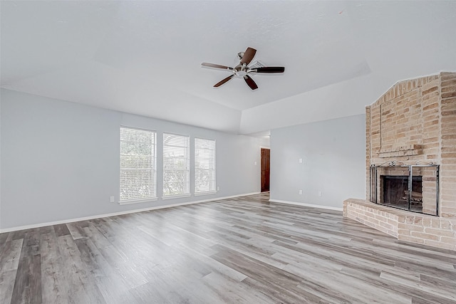 unfurnished living room featuring ceiling fan, a raised ceiling, light wood-type flooring, and a brick fireplace