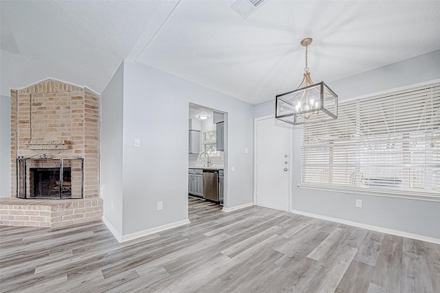 unfurnished living room with a fireplace, vaulted ceiling, sink, light hardwood / wood-style flooring, and a chandelier