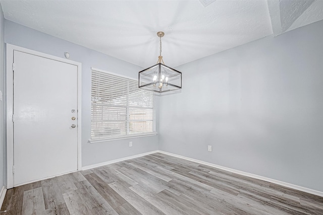 unfurnished dining area with light hardwood / wood-style flooring, a chandelier, and a textured ceiling