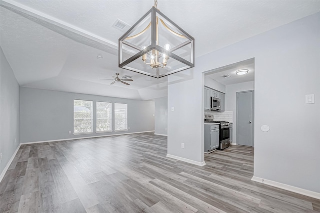 unfurnished living room featuring light wood-type flooring, a textured ceiling, a raised ceiling, and ceiling fan with notable chandelier