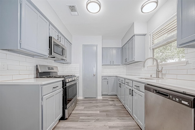 kitchen featuring gray cabinets, sink, light hardwood / wood-style floors, and stainless steel appliances