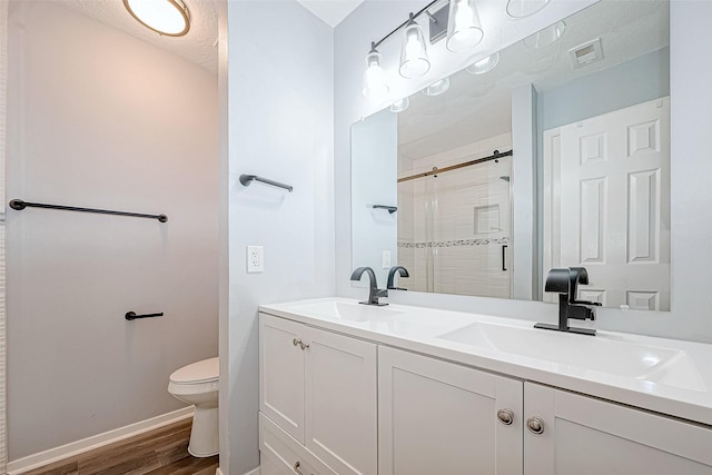 bathroom featuring hardwood / wood-style floors, a textured ceiling, toilet, vanity, and a shower with shower door