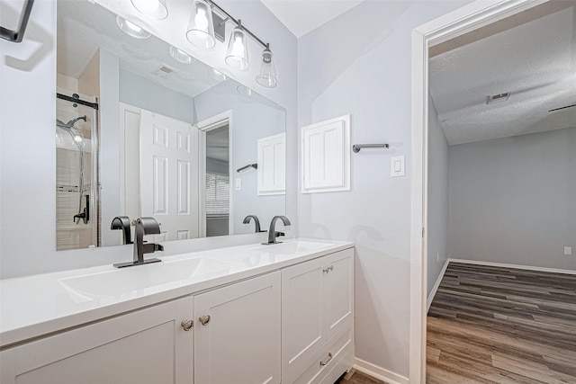 bathroom with hardwood / wood-style floors, vanity, a shower with shower door, and a textured ceiling