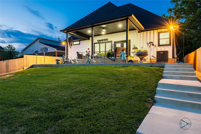 rear view of property featuring central AC unit and a lawn