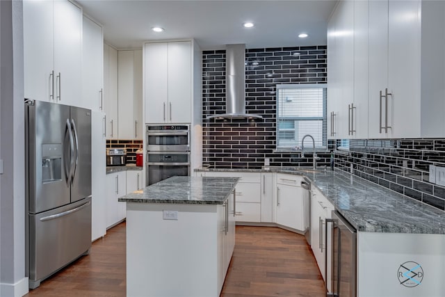 kitchen featuring appliances with stainless steel finishes, a center island, wall chimney range hood, and white cabinets