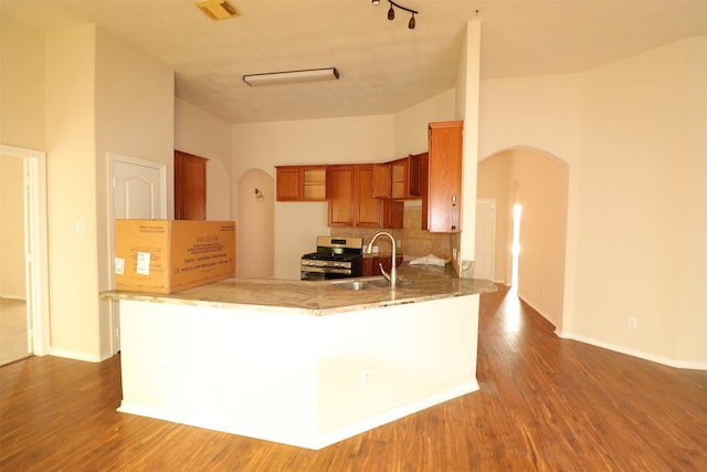 kitchen with high vaulted ceiling, stainless steel gas range oven, backsplash, track lighting, and sink