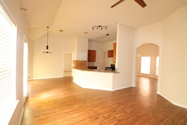 unfurnished living room with high vaulted ceiling, light hardwood / wood-style flooring, track lighting, ceiling fan with notable chandelier, and sink