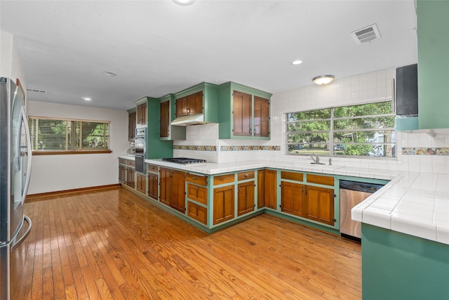 kitchen with appliances with stainless steel finishes, light hardwood / wood-style flooring, backsplash, and tile counters