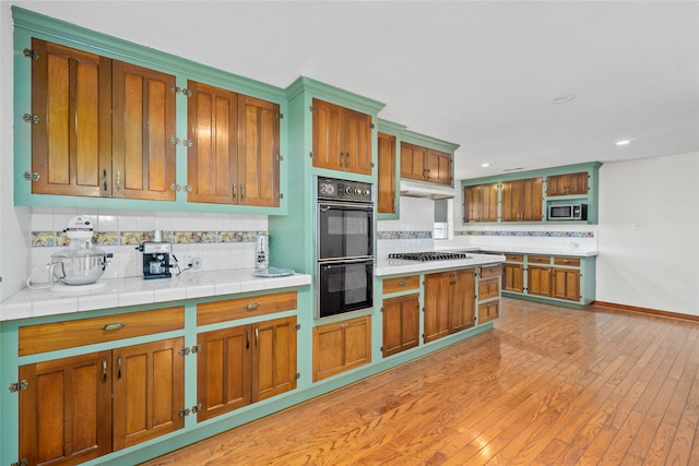 kitchen featuring backsplash, tile countertops, stainless steel appliances, and light wood-type flooring