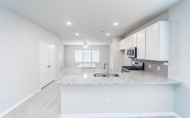 kitchen with kitchen peninsula, white cabinets, appliances with stainless steel finishes, light stone countertops, and sink