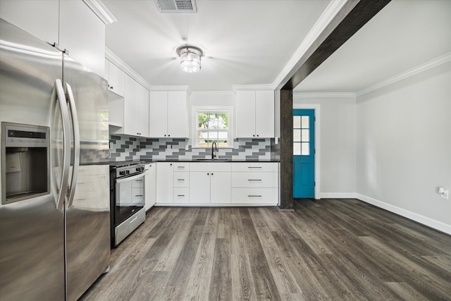 kitchen with appliances with stainless steel finishes, tasteful backsplash, dark wood-type flooring, ornamental molding, and white cabinets